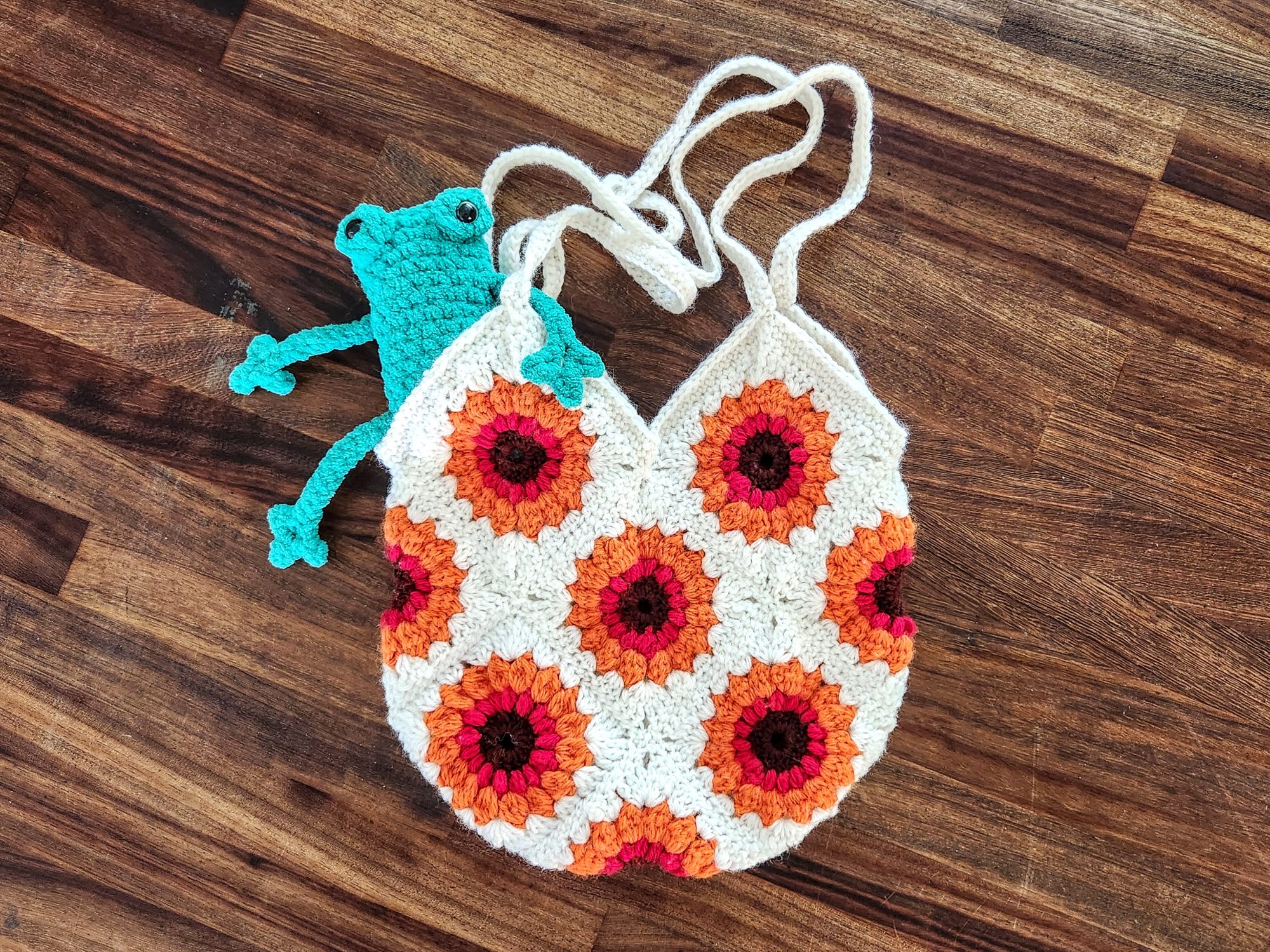 A cream, orange and berry granny-square tote bag with a sunflower motif and a small teal frog