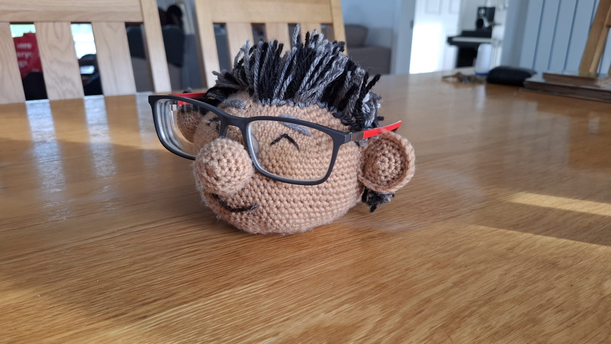 A crocheted character head that holds a pair of glasses on its nose